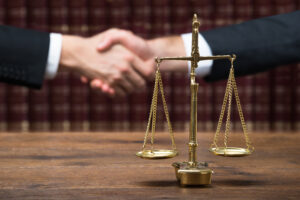 Family Lawyer Alameda County, CA with a justice scale on wooden table with lawyer and client shaking hands in background in front of law books